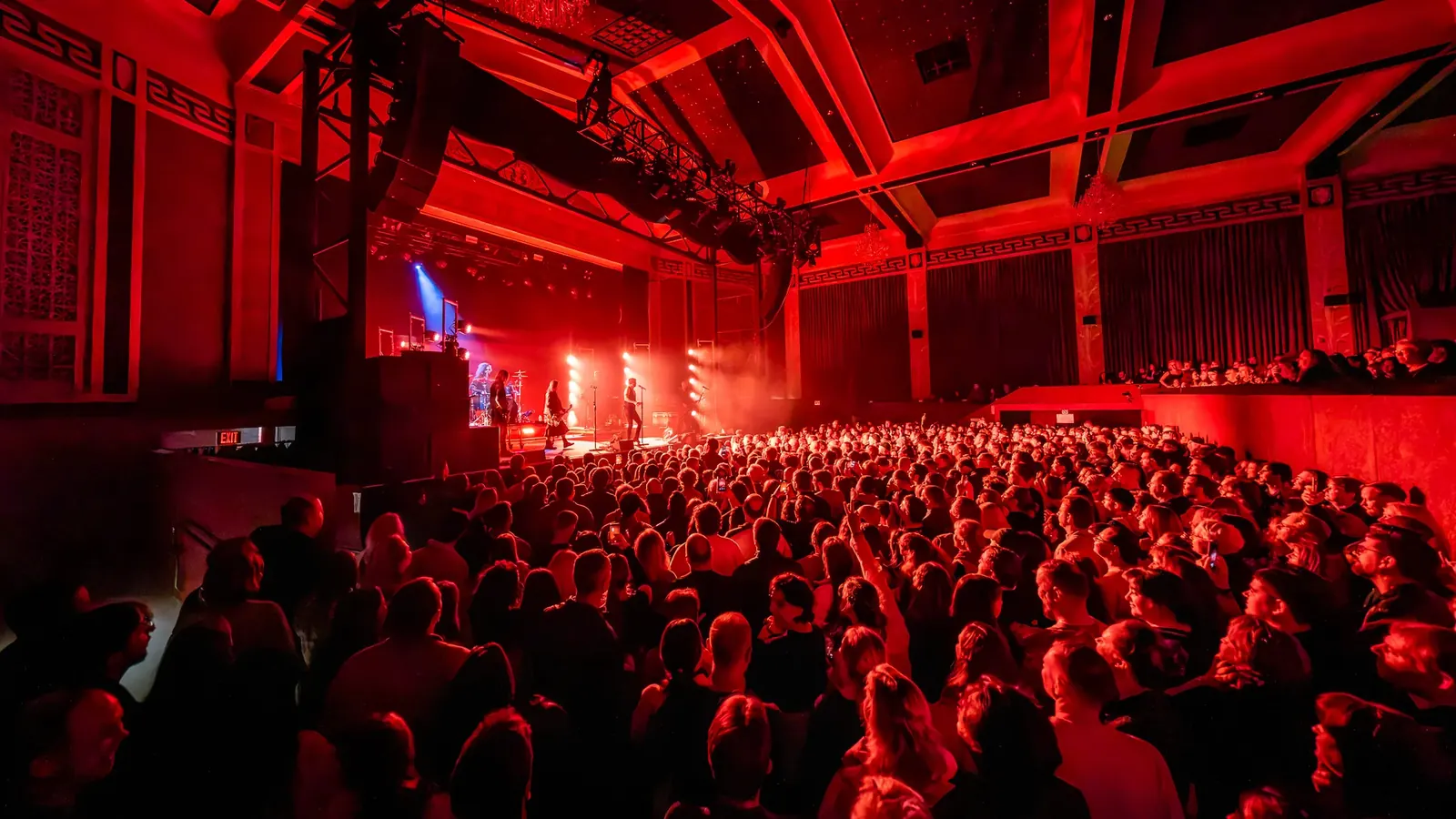 A red-lit concert hall filled with an audience